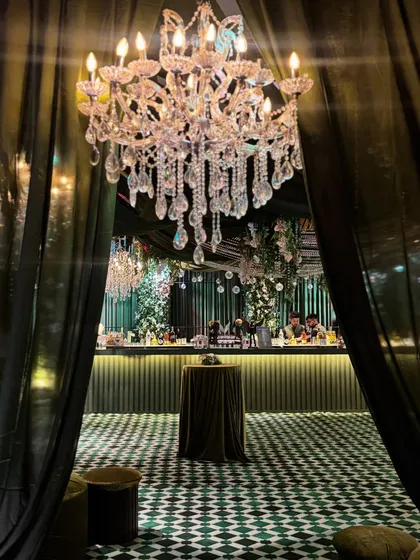 A dramatic entrance to the enchanted forest bar area. A large crystal chandelier hangs between deep green curtains, inviting guests into a space of elegance and mystery.