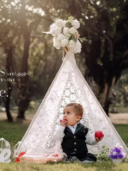 Playdates and giggles. A dapper little boy enjoys a snack during his outdoor first birthday photoshoot in our lace teepee.