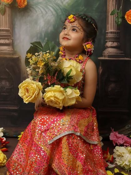 Little Radha holding a bouquet of flowers, looking up with a serene expression. This portrait captures the beauty and devotion associated with Radha, perfect for a festive photoshoot.