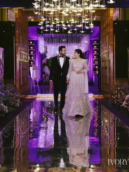 The couple's grand entrance into their reception hall. The reflective floor and dramatic chandeliers create a stunning visual, making them look like royalty.