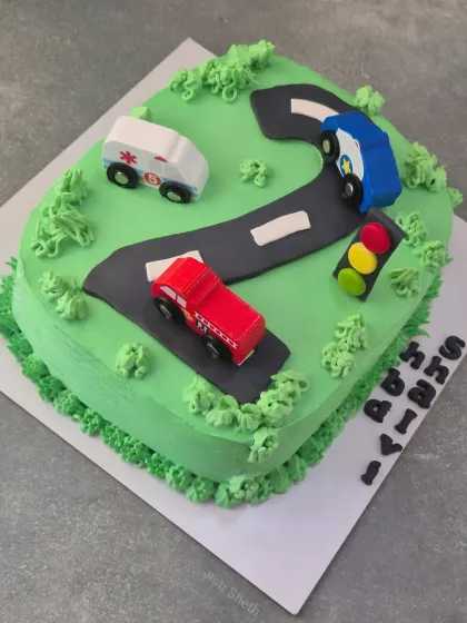 A fun number '2' cake for a toddler's birthday, themed around cars and traffic. The road, cars, and traffic light are all handcrafted details on a whipped cream base.