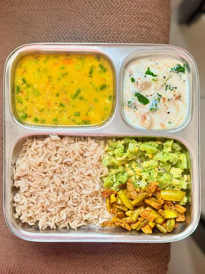 This plate features brown rice, mixed vegetable dal, and a variety of sautéed vegetables with raita. It's a colorful and nutrient-dense meal.