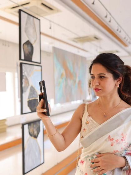 A guest capturing a photo of an artwork at our gallery, with paintings from 'Nature's Symphony' in the background.