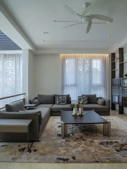 This sophisticated living room uses a muted color palette and rich textures to create a comfortable and stylish space. The large, open-backed shelving unit serves as both storage and a display for curated objects.