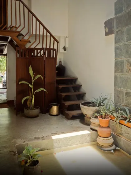The courtyard area of the ancestral home, featuring a traditional wooden staircase, stone walls, and an abundance of potted plants that bring life to the space.