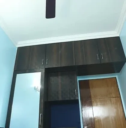 This bedroom storage solution includes a dark wood-finish wardrobe with an integrated mirror and overhead loft cabinets to maximize vertical space.