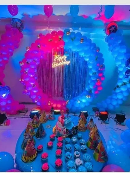 A 'boy vs girl' or twins-themed party with a split pink and blue design. The decoration features two circular balloon arches in contrasting colors, with a shared 'Happy Birthday' neon sign.