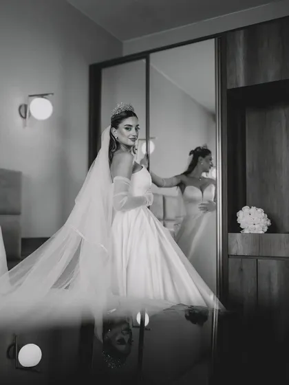 A bride in a beautiful white wedding gown looks at her reflection in a mirror, captured in a timeless black and white style. This image shows my approach to bridal photography, focusing on quiet, elegant moments.