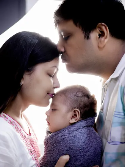 A classic and emotional family pose. The parents gently kiss their newborn's forehead, creating a beautiful silhouette filled with love and tenderness.