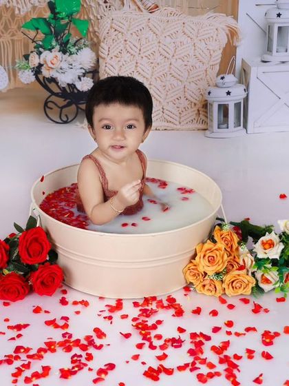 A baby enjoys a milk bath with red rose petals, set against a rustic boho backdrop. This type of session creates soft, beautiful, and unique portraits.