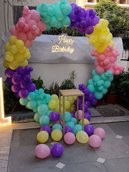 A bright and cheerful first birthday decoration for an outdoor space. I used a ring of rainbow-colored balloons, a neon sign, a cake pedestal, and a marquee number '1'.