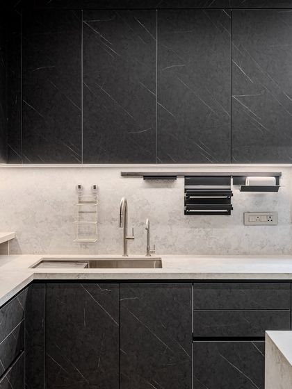 A close-up of the sink area, where the dark, veined cabinet fronts are paired with a light quartz countertop and a practical rail system for utensils.