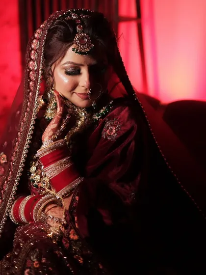 A dramatic, artistic shot of the bride. The red lighting enhances her maroon outfit and the smokey eye makeup, creating a powerful and modern bridal portrait.