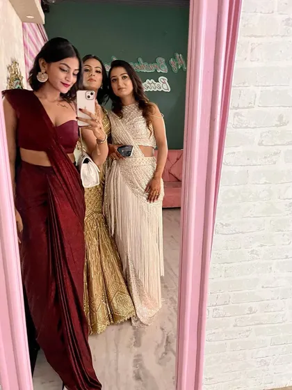 A mirror selfie with friends at a wedding event. I'm wearing a deep maroon pre-draped saree with a modern bustier, showcasing a chic and contemporary approach to Indian festive wear.