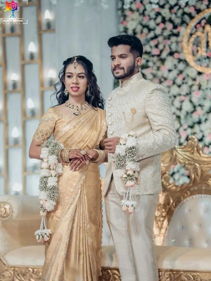 A formal portrait of the couple on their engagement stage. Their coordinated golden outfits and the grand decor create a look of pure opulence.