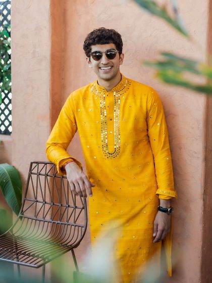 A bright and cheerful look for the Haldi ceremony. This brother of the bride is wearing a vibrant yellow kurta with mirror work around the neckline, perfectly fitting the festive and sunny theme of the event.
