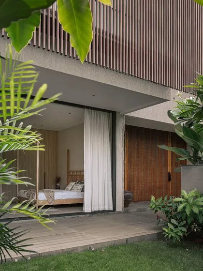 A guest bedroom that opens directly onto a private garden deck. The four-poster bed and light wood tones create a calm and airy atmosphere, embodying the tropical modern style.
