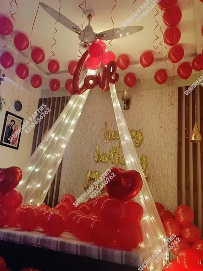 A romantic bedroom decoration to surprise your loved one on their birthday. This intimate setup features a canopy made of soft fabric and fairy lights over the bed, with red heart-shaped balloons and a "Love" foil balloon to create a memorable moment.