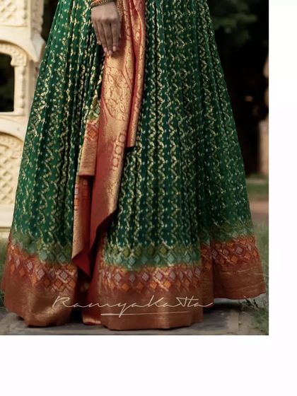 A close-up of the rich green brocade fabric with its classic Bandhini pattern and golden zari work.
