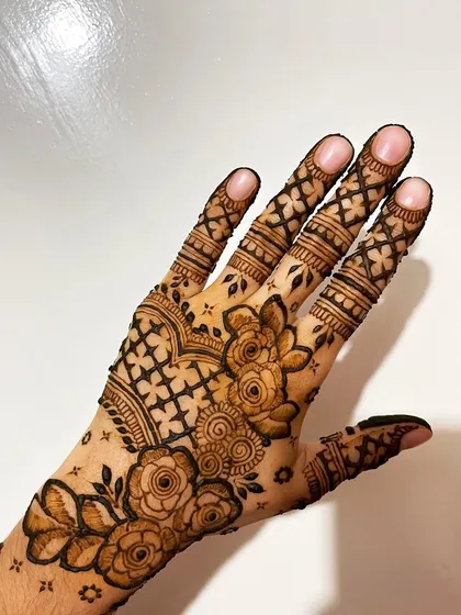 A beautiful Eid henna design with a mix of roses and a crisscross pattern on the fingers and hand.