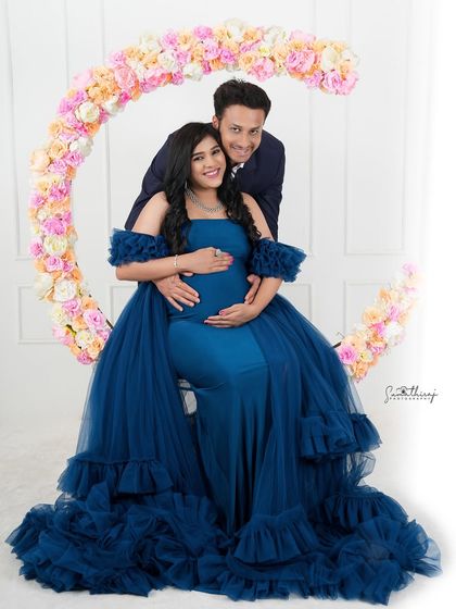 A joyful couple portrait with a floral moon prop. The deep blue gown and their happy expressions create a magical and celebratory scene.