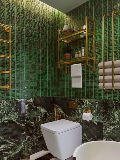 A detail shot of the green master bathroom, focusing on the gold towel warmers and storage racks against the textured green tile and dark marble.