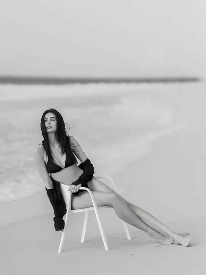 Bold, beautiful, and breathtaking. A striking black and white portrait of a model in a bikini, seated on a chair on a Dubai beach, exuding pure confidence.