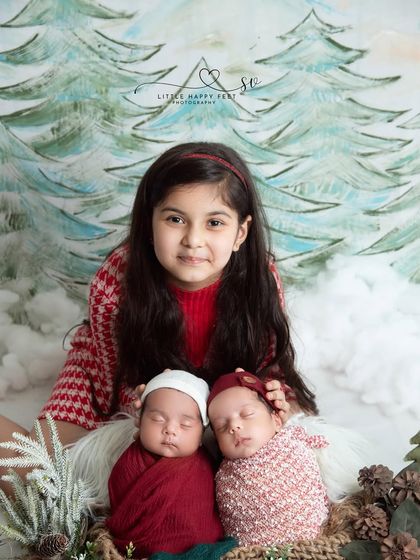 A festive family portrait! This big sister is so proud to pose with her new twin siblings in a cozy Christmas-themed setup.