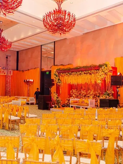 The overall indoor setup for the Haldi, where the vibrant yellow of the chair covers and stage curtains is contrasted beautifully with dramatic red chandeliers.
