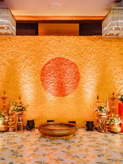 A massive wall of marigolds with a contrasting red circle creates a powerful and artistic backdrop for this Haldi ceremony. The design is both traditional in its use of flowers and modern in its graphic composition.