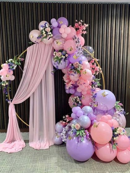 An elegant circular hoop decorated with pink and purple balloons, artificial flowers, and draped fabric, creating a sophisticated photo backdrop.