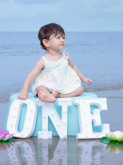 A serene first birthday portrait at the beach. Using the calm ocean as a natural backdrop, this simple setup with 'ONE' letters creates a beautiful and memorable image to mark this special milestone.