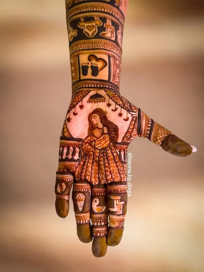 A single-hand close-up of a Godh Bharai mehendi, showing a detailed portrait of an expecting mother. The fingers include small, meaningful symbols like a duckling and an ice cream cone.