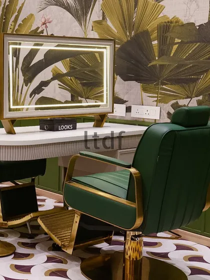 A detail shot capturing the essence of the salon's design. The custom-lit mirror reflects the tropical wallpaper, while the gold-accented chair stands ready, promising a moment of luxurious self-care.