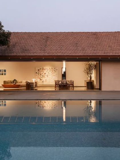 A restrained and elegant holiday home we designed in Alibaug, seen here at dusk. The living pavilion opens up to a serene pool, reflecting the warm interior light and the traditional tiled roof.