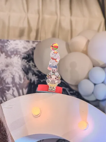 A close-up on a small, charming detail from the carnival setup: a tiny cutout of circus performers balancing.