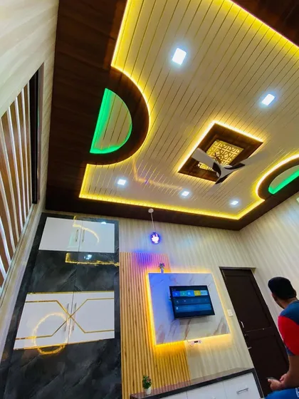 Your home can be a work of art. This living room features a multi-level PVC ceiling with both warm and cool LED lighting, a custom TV unit with marble-finish panels, and modern WPC louvers. Every detail is planned to create a unique and functional space.