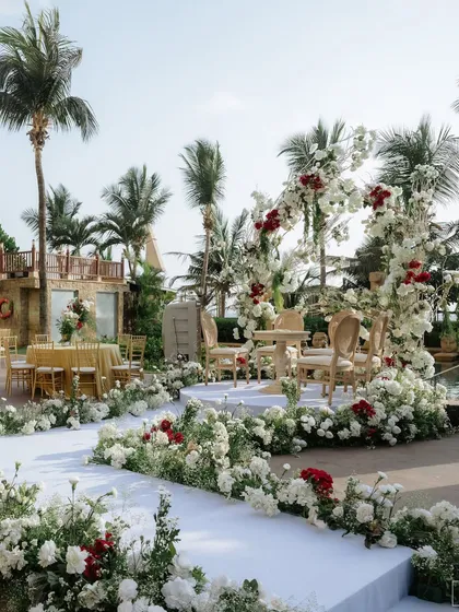 Set against the serene backdrop of the sea, this wedding ceremony arch is a picture of timeless romance. I wove together a tapestry of lush white hydrangeas and roses, punctuated with deep red blooms for a touch of passion. The design frames the couple and the ocean, creating a breathtaking setting for their happily ever after.