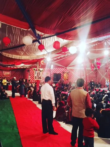 This photo captures the atmosphere of a large satsang event I decorated. You can see the scale of the gathering, with a fully decorated tent and organized seating for a large number of people.