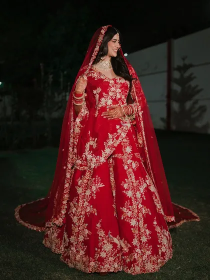 A full-length portrait of the bride, Anisha, in her magnificent red wedding lehenga. Her confident smile and the grandeur of her outfit create a stunning image.
