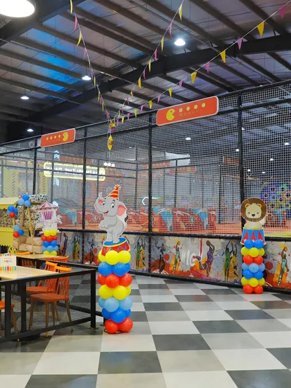 A wide view of the dining and play area decorated for a carnival party. Themed balloon columns with elephant and lion characters add to the fun.