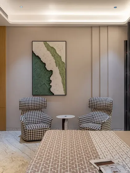 A close-up of the cozy reading corner in the master suite, featuring statement houndstooth chairs and a textured abstract artwork. This space is designed for quiet contemplation.