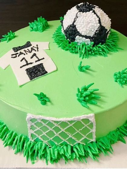 A black forest cake for a football champ. The cake is designed to look like a soccer field, complete with a goal, a jersey, and a football.