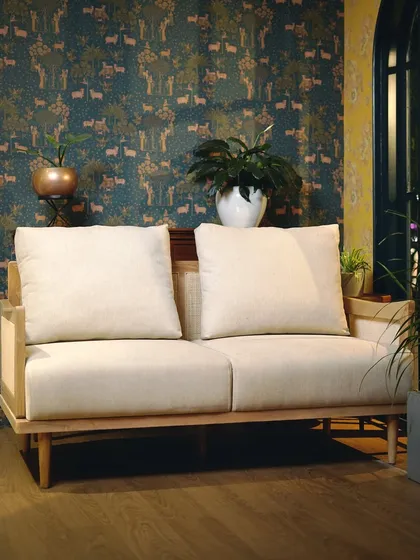 Our signature two-seater sofa combines a solid Teak wood frame with delicate, handwoven cane panels. This piece exemplifies our commitment to blending traditional craftsmanship with clean, modern lines for a timeless aesthetic.