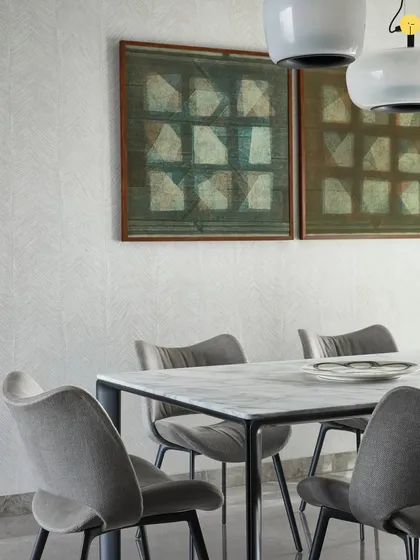 The dining space at 'Pad by the Bay' features elegant chairs and a minimalist table, allowing the focus to remain on the artwork and the view. The wallpaper adds a subtle texture, enhancing the room's quiet sophistication.