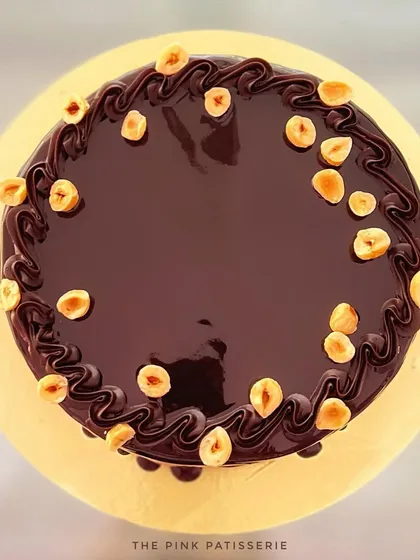 A top-down view of the hazelnut crunch cake, showing the glossy chocolate glaze and scattered hazelnuts.