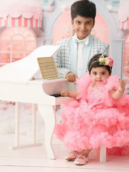 A charming portrait of a brother and his baby sister at a miniature white piano. This shot captures the sweet dynamic between siblings in one of our imaginative studio settings.