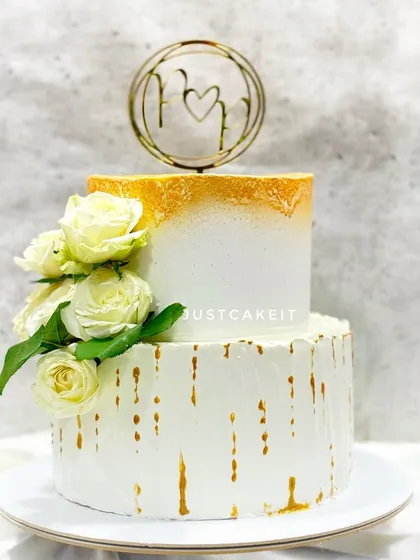 An elegant engagement cake with a gold-dusted top tier and a white drip on the bottom. The fresh white roses and custom topper complete the sophisticated look.