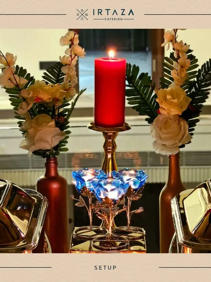 A detail shot of a centerpiece on a serving table. A tall red candle in a golden holder is surrounded by elegant blue crystal votives and white flowers, showcasing my attention to even the smallest decorative details.