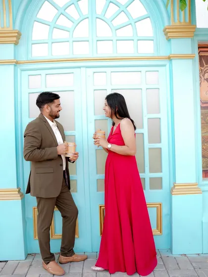 A playful moment sharing a drink against a vibrant blue door, reminiscent of a European street. The woman's bright red dress pops against the cool tones, creating a lively and stylish pre-wedding photo.